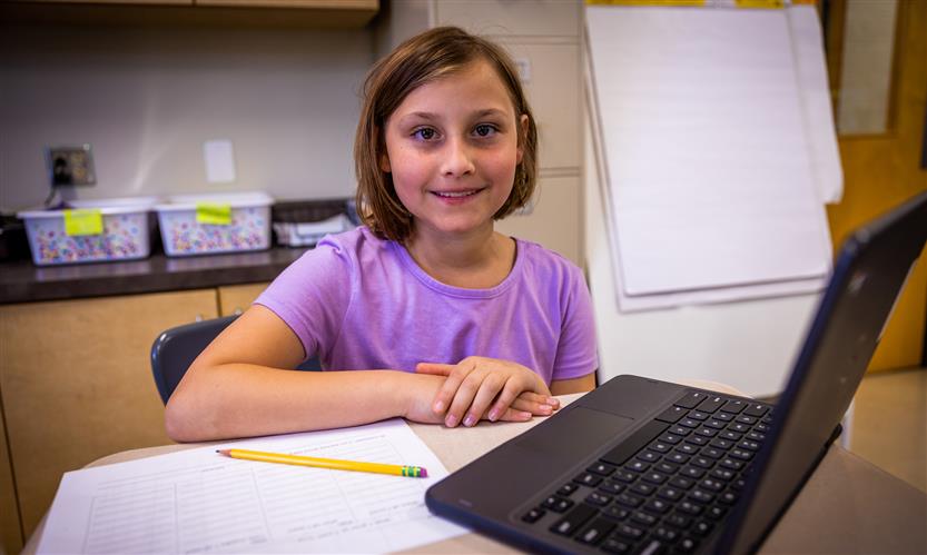 A girl with short brown hair and wearing a purple shirt smiles